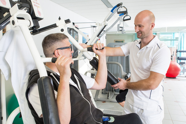 Ein Therapeut leitet einen Patienten an einem Sportgerät an