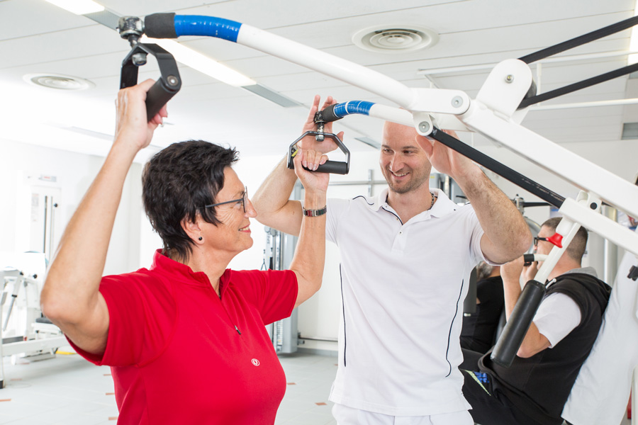 Ein Therapeut leitet eine Patientin an einem Sportgerät an